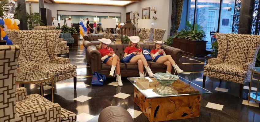 Three girls dressed as cowgirls flop down on a couch in a luxury hotel